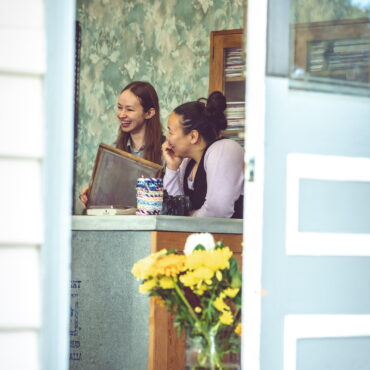 Half open blue and white door shows through to two people smiling at the front counter of shop